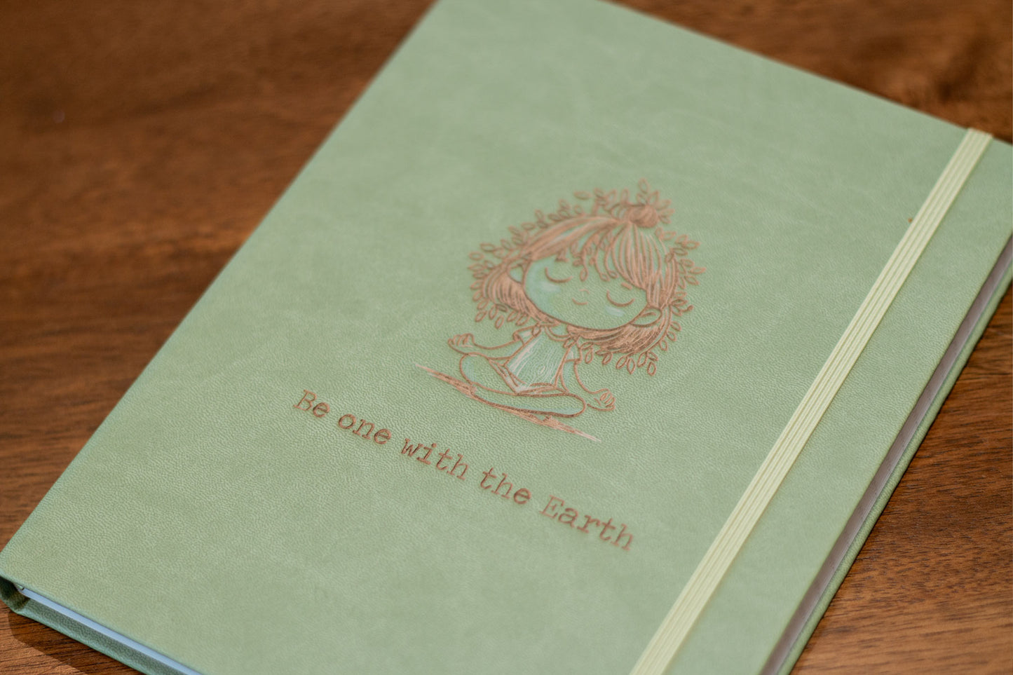 Customizable Meditation Journal featuring nature-inspired artwork by Holly Hatam, depicting a girl meditating with leaves for hair and tree-trunk textured clothing. Personalizable meditation journal with exclusive artwork, durable PU leather cover, and customizable engraving option.