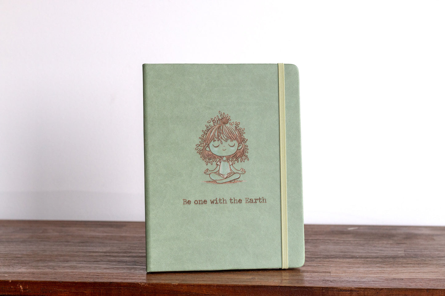 Customizable Meditation Journal featuring nature-inspired artwork by Holly Hatam, depicting a girl meditating with leaves for hair and tree-trunk textured clothing. Personalizable meditation journal with exclusive artwork, durable PU leather cover, and customizable engraving option.